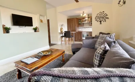 Laurel Cottage's lounge at Mill Farm Leisure with a plush grey sofa, wooden coffee table, and glimpses of the adjacent kitchen.